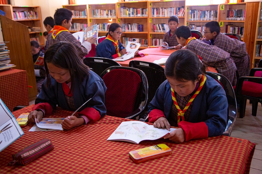 Children in a Bhutanese school sit at desks looking at books.