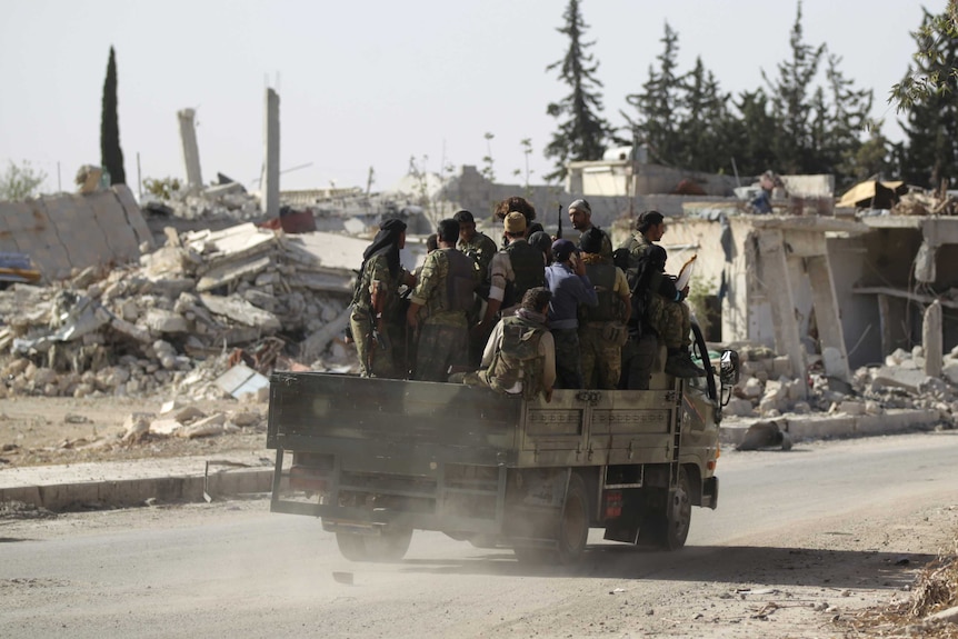 Rebel fighters drive past damaged buildings in al-Rai town, northern Aleppo