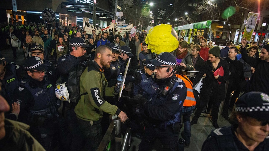 A protester is surrounded by police as a tram approaches on collins street