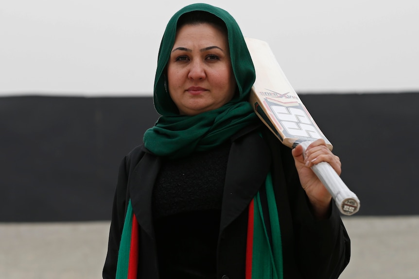 Afghan woman Diana Barakzai, founder of the Afghanistan women's cricket team, stands in a stadium in Kabul holding a bat.