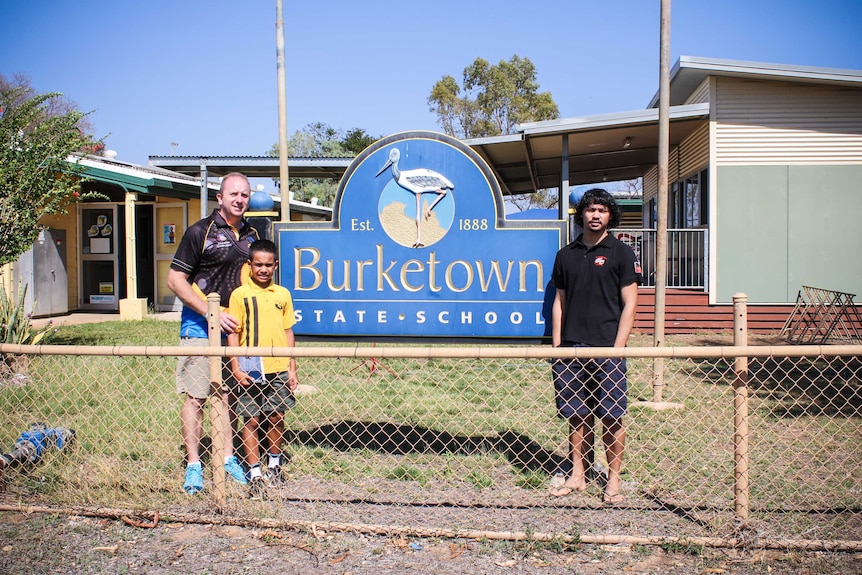 Three people standing out the front of the 'Burketown State School' sign.