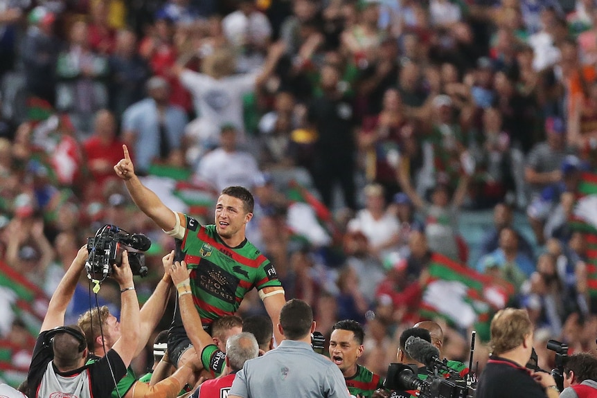 Sam Burgess points to the air as he rides on South Sydney Rabbitohs teammates' shoulders after the 2014 NRL grand final.