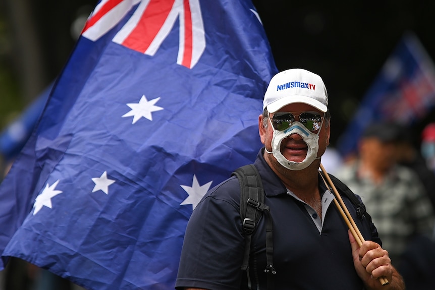 A man wears a mask with a hole cut out of it and carries the Australian flag