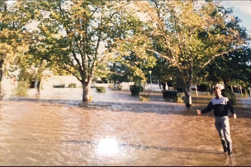 A man standing in floodwaters in front of trees