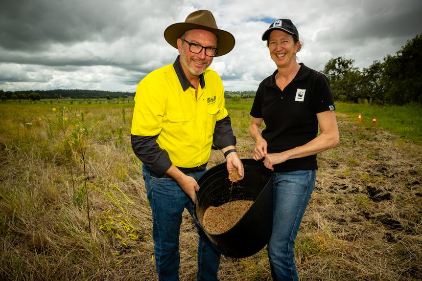 Two people smiling with a bucket of seed mix