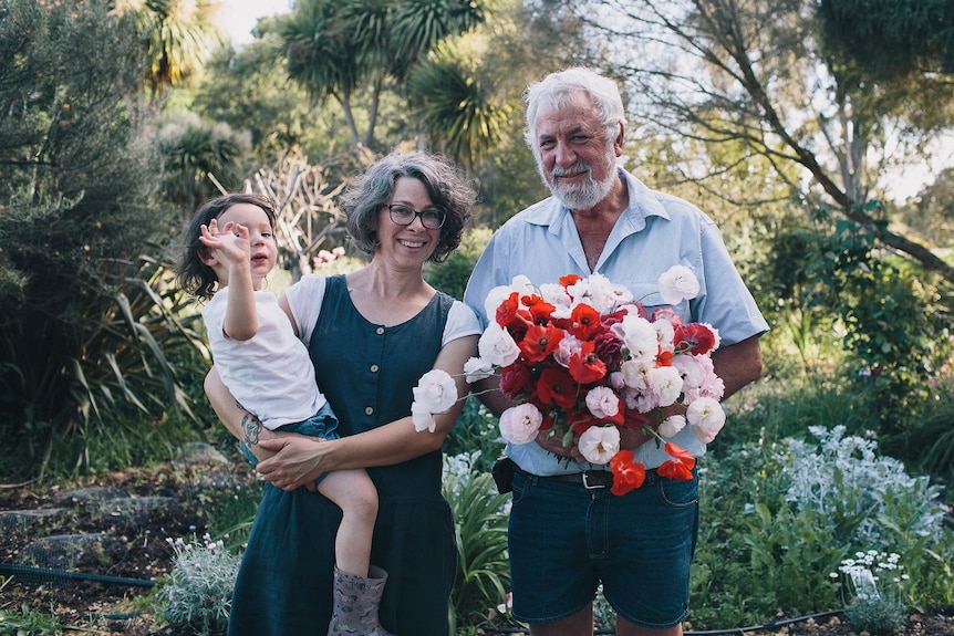 A man and woman and a child  standing with a bunch of flowers in a garden.