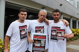 Three men stand with flyers featuring the face of a missing man.