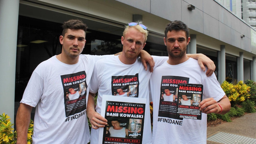 Three men stand with flyers featuring the face of a missing man.