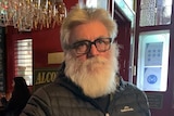 A man with a beard and glasses leans on a bar.