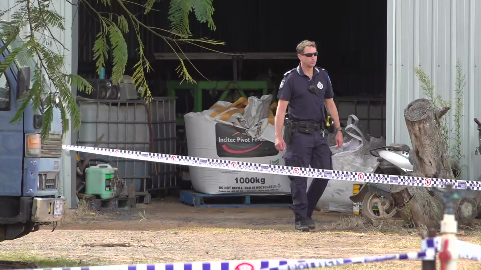 A uniformed policeman near a large shed that has been cordoned off with tape.