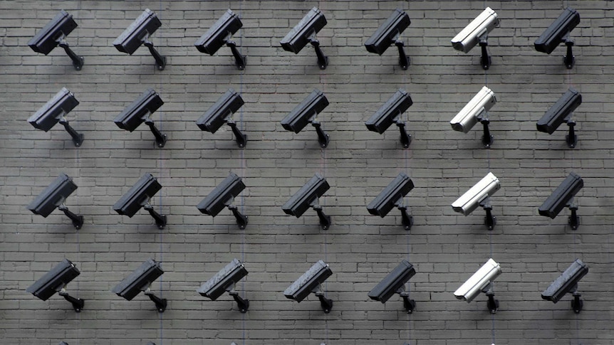 Several rows of surveillance cameras against a brick wall.