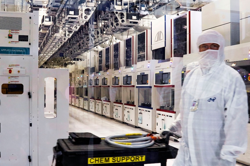 Une personne en EPI blanc complet se tient dans une rangée d'appareils de fabrication de haute technologie blancs.