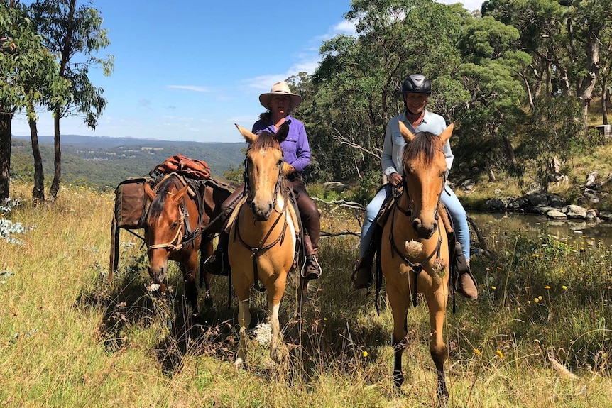 Two women ride horses near a river in remote New South Wales.