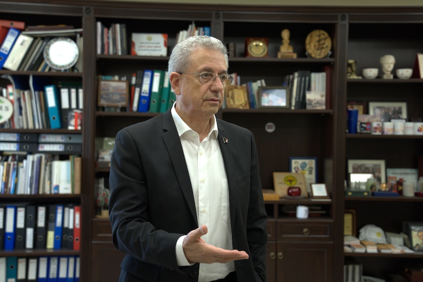 A man gestures in front of a bookcase