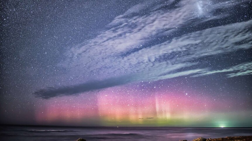 Starry night with pink, green, yellow lights over sea