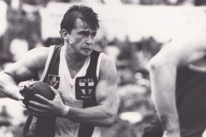 A man in a St Kilda guernsey holds the ball and runs.
