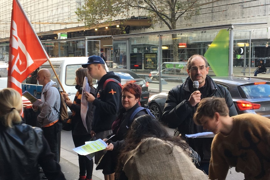 A group of protesters stand hold flags and signs outside Victoria University's city campus.