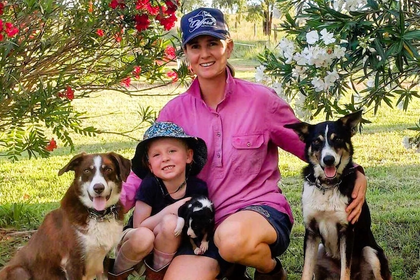 A lady wearing a long sleeved pink shirt with a young child and two working dogs and a pup.