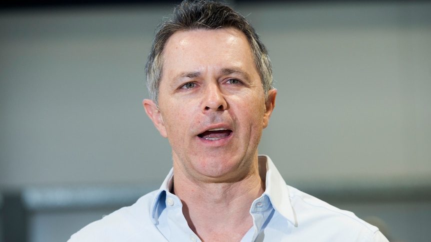 A close shot of a man wearing a blue button up shirt and speaking. 