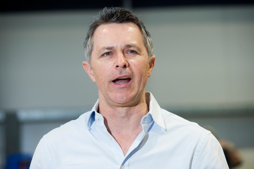 A close shot of a man wearing a blue button up shirt and speaking. 