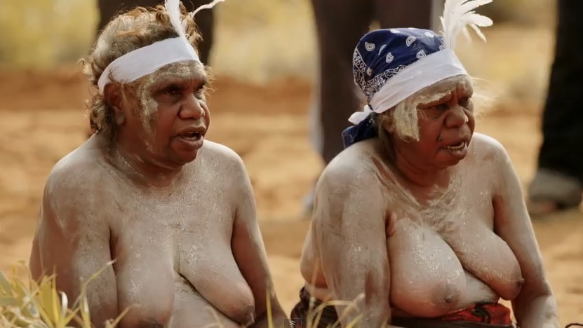 A group of older Indigenous women with their breasts bared in ochre painting.