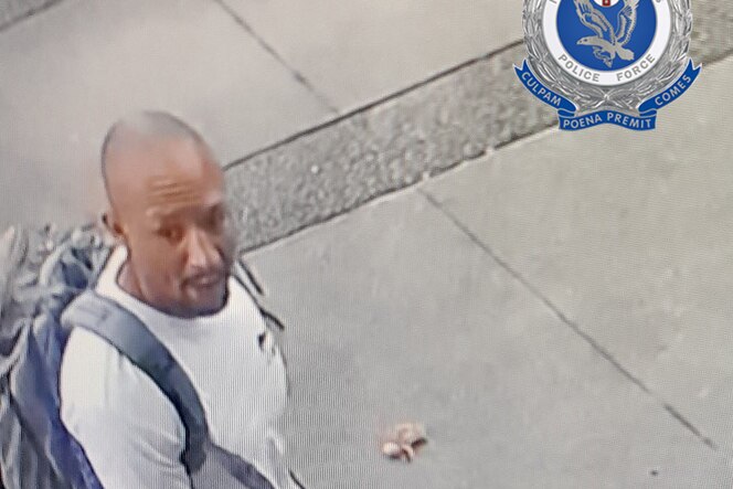 A CCTV image of a man with a shaved head, wearing a light-coloured T-shirt and a backpack.