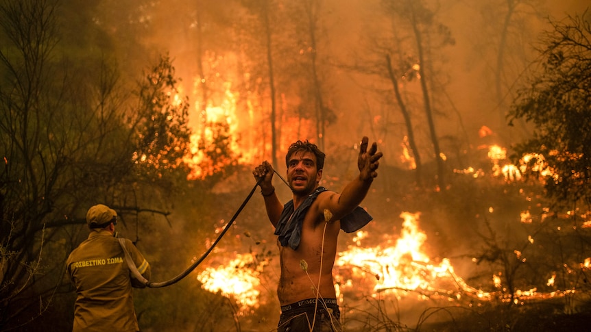 A local resident holds a hose as a firefighter aims water at a massive forest blaze