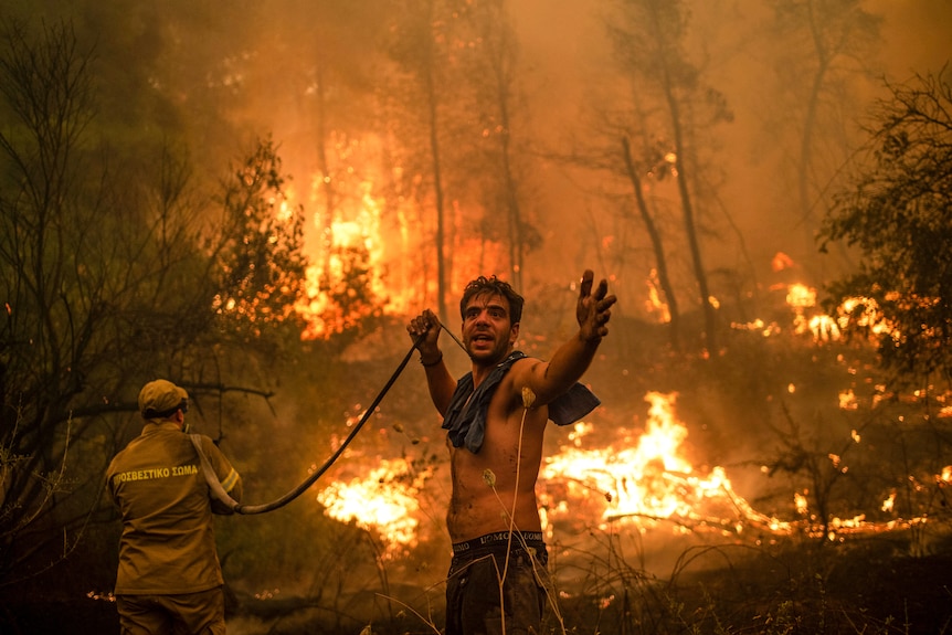 A local resident holds a hose as a firefighter aims water at a massive forest blaze