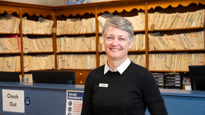 A women stands in front of medical files and smiles at the camera