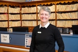 A women stands in front of medical files and smiles at the camera