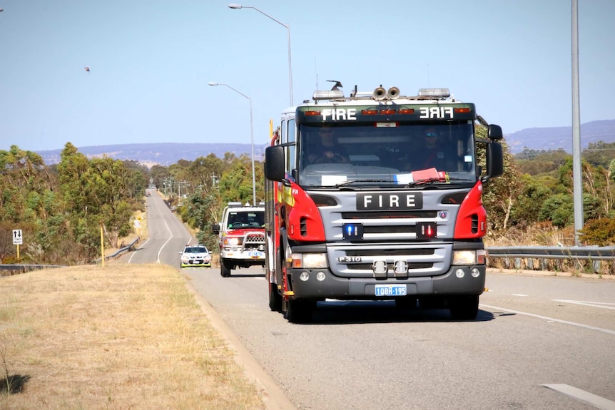 A fire truck drives down a country road followed by a police car