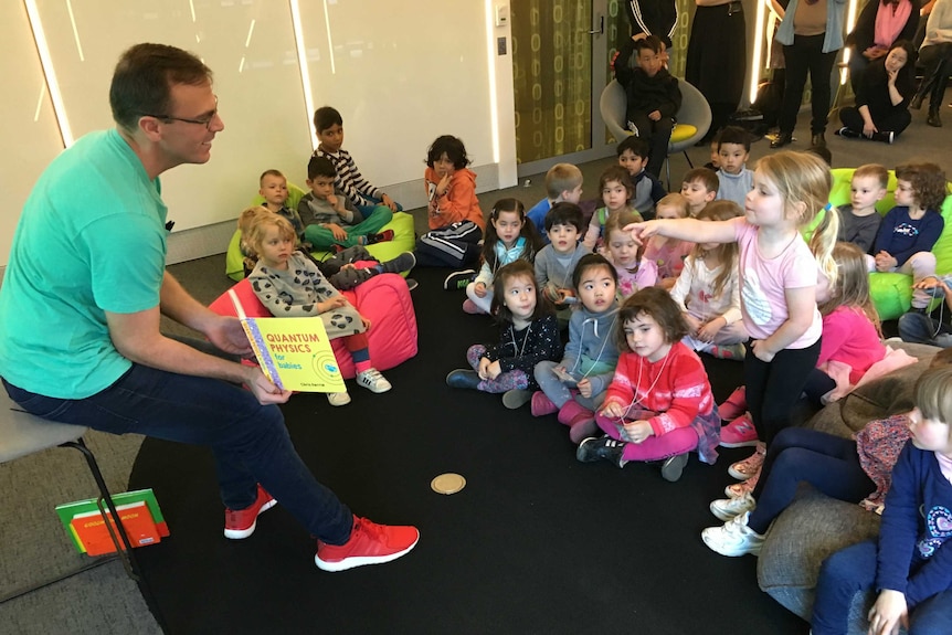 Quantum physicist Chris Ferrie holds up a book in front of a small group of young children.