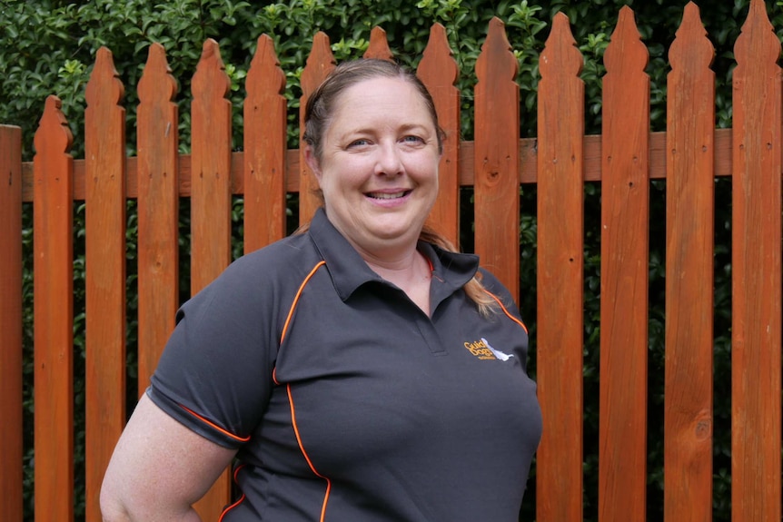 A woman in a uniform stands in front of a fence.