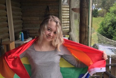 A teenage girl with blonde hair wrapped in a rainbow flag