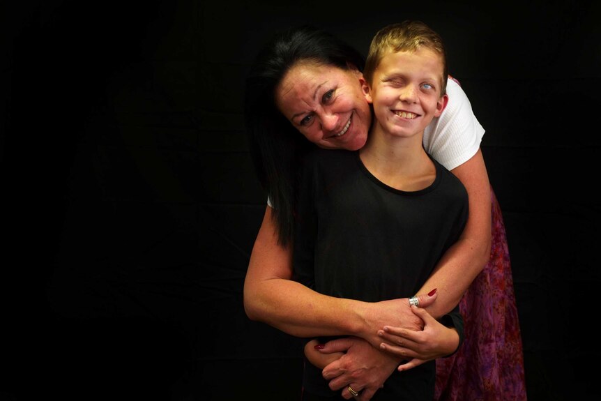 A woman and her young son stand smiling before a black background.