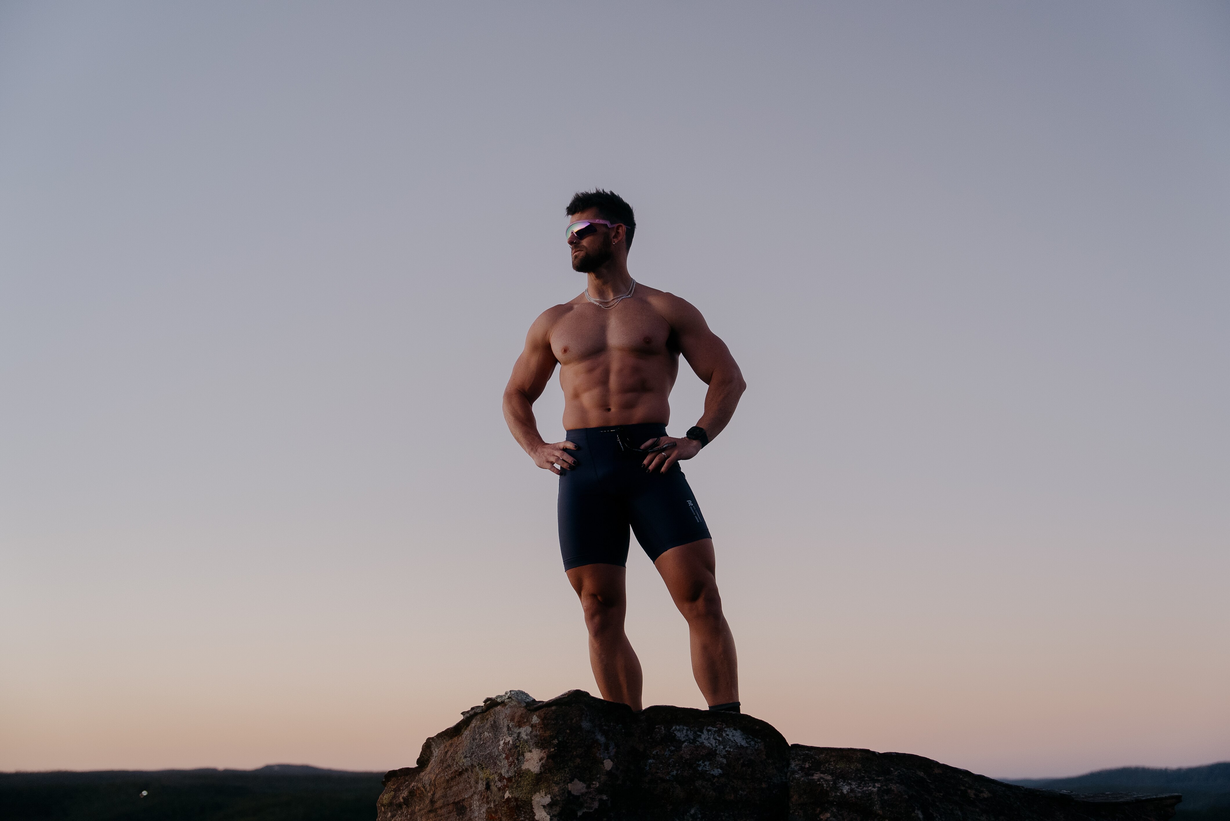 Nathan McCallum, sin camisa, se encuentra encima de un acantilado mientras se pone el sol.