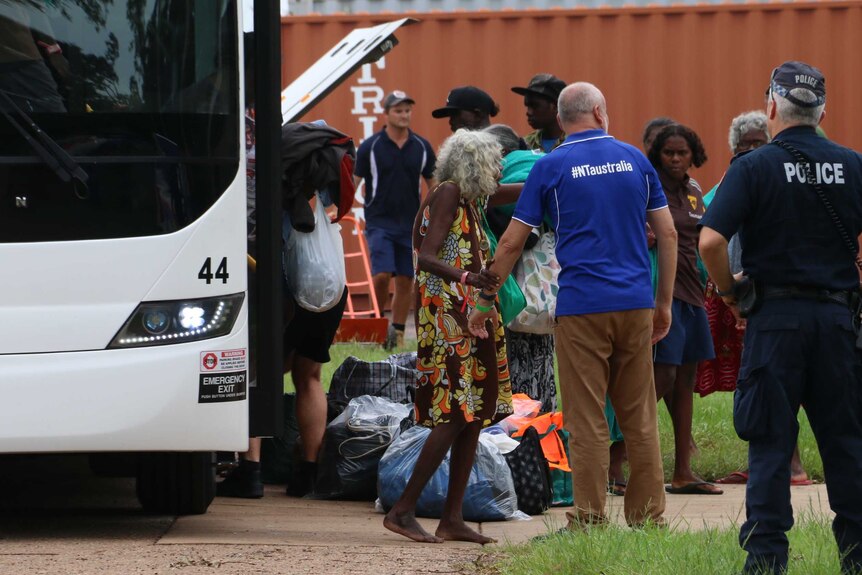 A number of people are helped off a bus, carrying personal items.