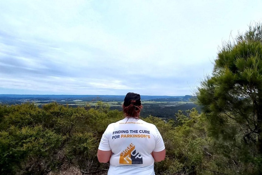 a woman stands looking out at the view from a mountainside 