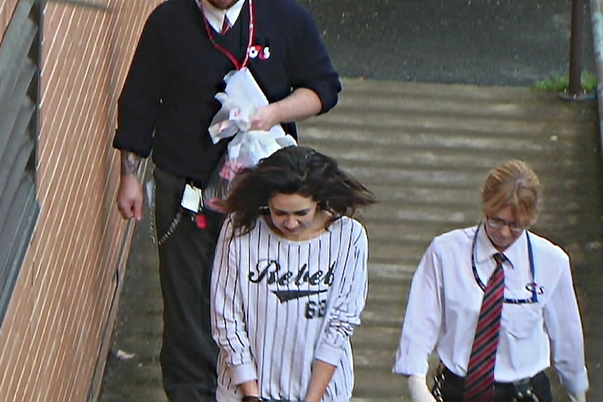 Court officers escort a woman in handcuffs.