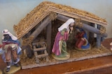Three wise men in robes along with Mary in a red rob inside a straw hut.