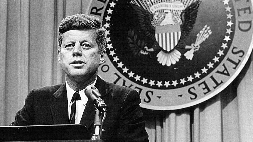 JFK at a podium, the presidential seal is behind him