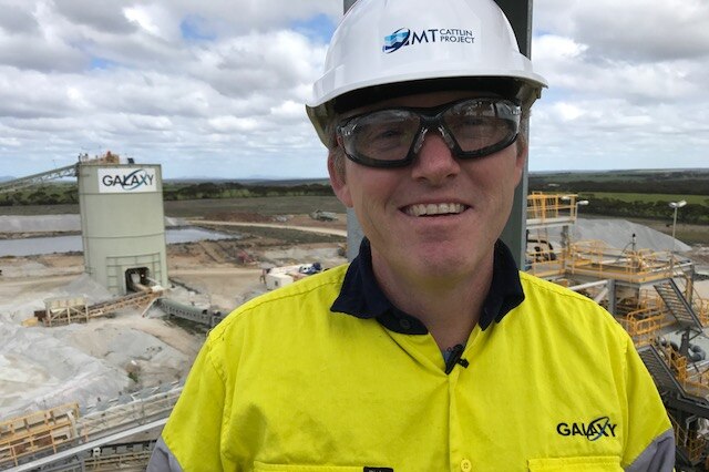 Brian Talbot wearing a safety helmet and glasses with the mine site in the background.