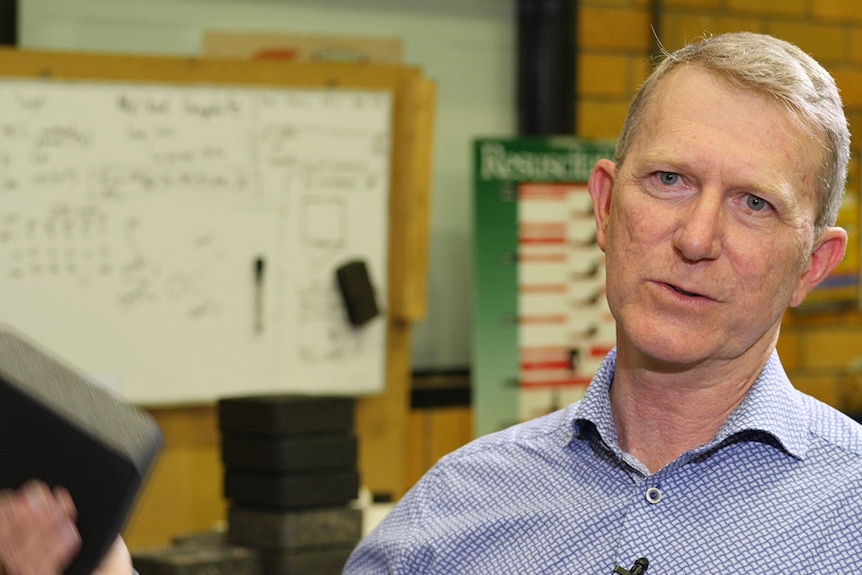 Still frame from a video interview in a university lab workshop with a man holding a dark brick