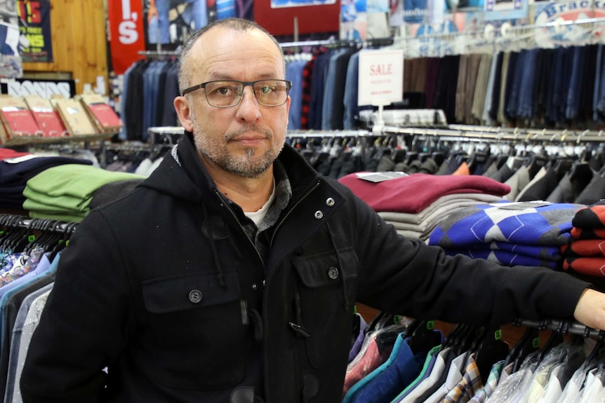 Warren Menswear owner Sam Pangiarella stands in his store surrounded by clothing racks.