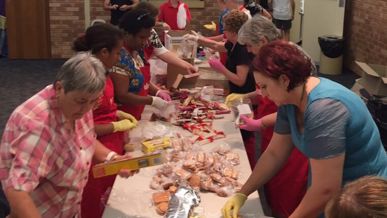 A group of women prepare food packs at a long table.