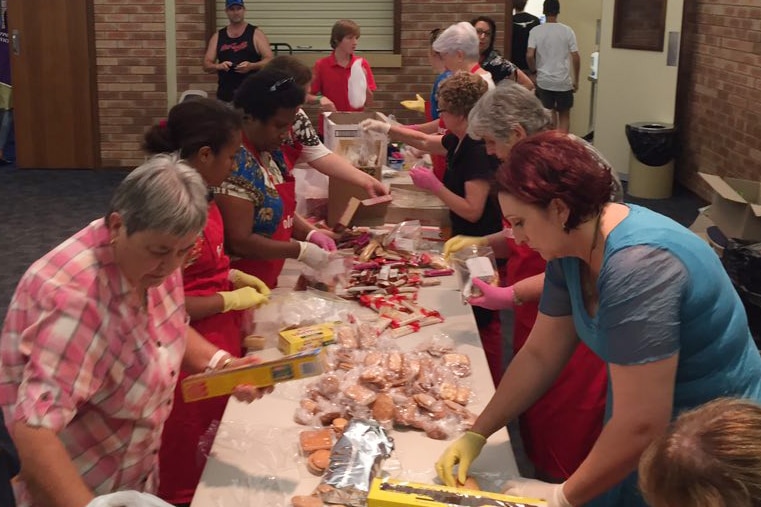 A group of women prepare food packs at a long table.