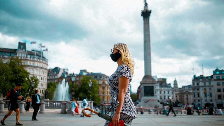 A woman in a black face mask walks through Trafalgar Square