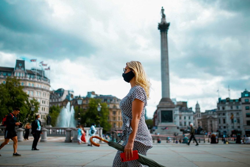 A woman in a black face mask walks through Trafalgar Square