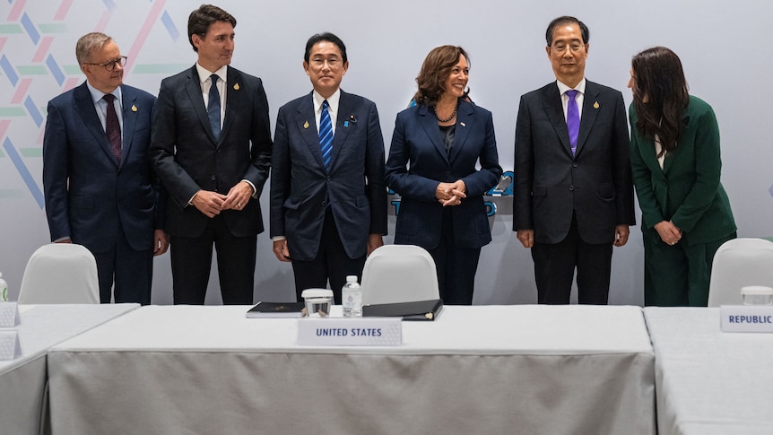 The leaders stand in a line behind a table. 