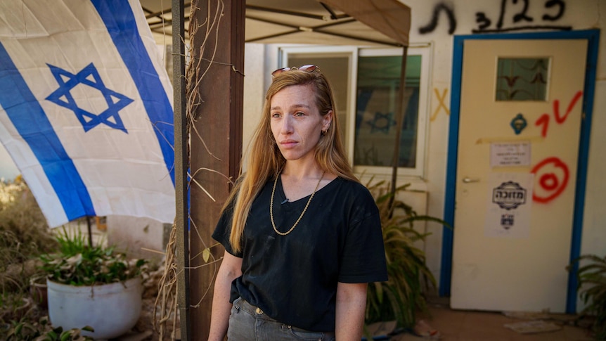 A young woman with long blonde hair stands by an Israeli flag 